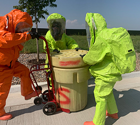 Three Greeley firefighters handling a drum of hazardous material